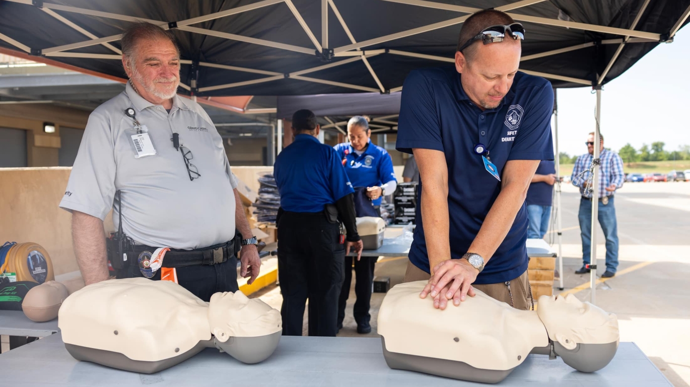 A safety officer practices CPR on a manikin while others look on.