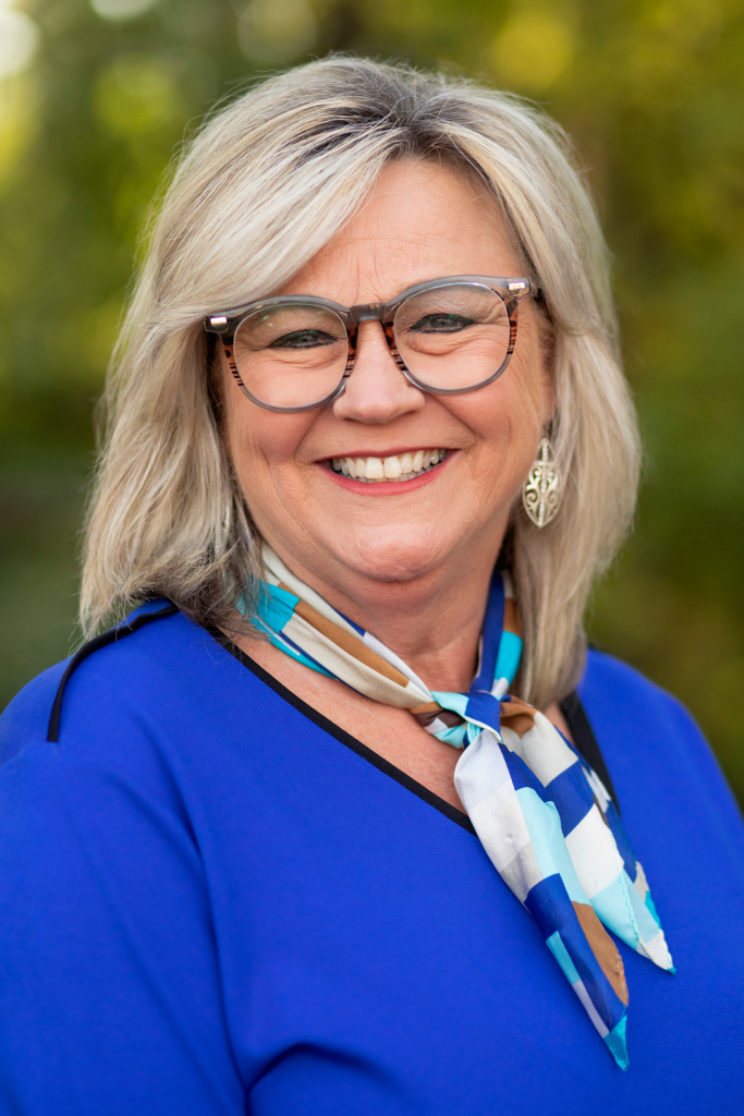 Headshot of CPN Director of Employee Advocacy, Kelley Francen. Francen wears a brilliant blue blouse with accenting silk scarf. She has shoulder-length blonde hair and her eyes smile behind large brown glasses frames.