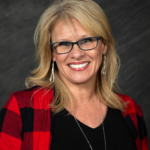 A headshot of CPCDC Commercial Loan Officer and Certified Credit Counselor, Felecia Freeman. Freeman wears a red plaid cardigan that pops against her black shirt. Her blonde hair falls in styled curls to her shoulders.