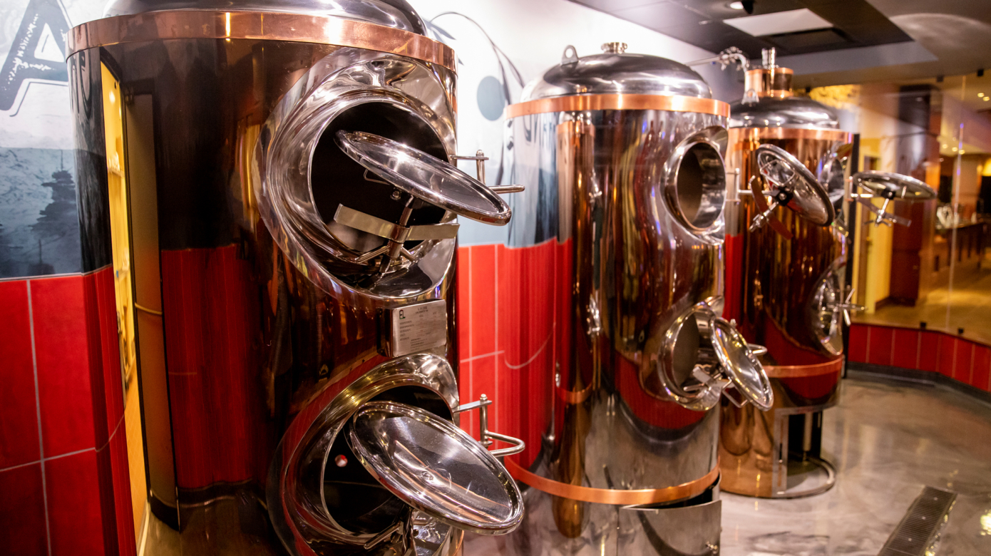 A row of three beer brewing machines reflecting the warm light of the interior of the Grand Casino.