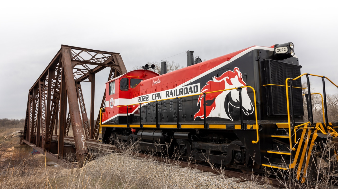 CPN's newly-refurbished switch engine, featuring a bold design of red, black, white, and yellow, and Iron Horse Industrial Park's logo of a horse whose mane is blowing in the wind, crosses a rail bridge near Tribal headquarters.