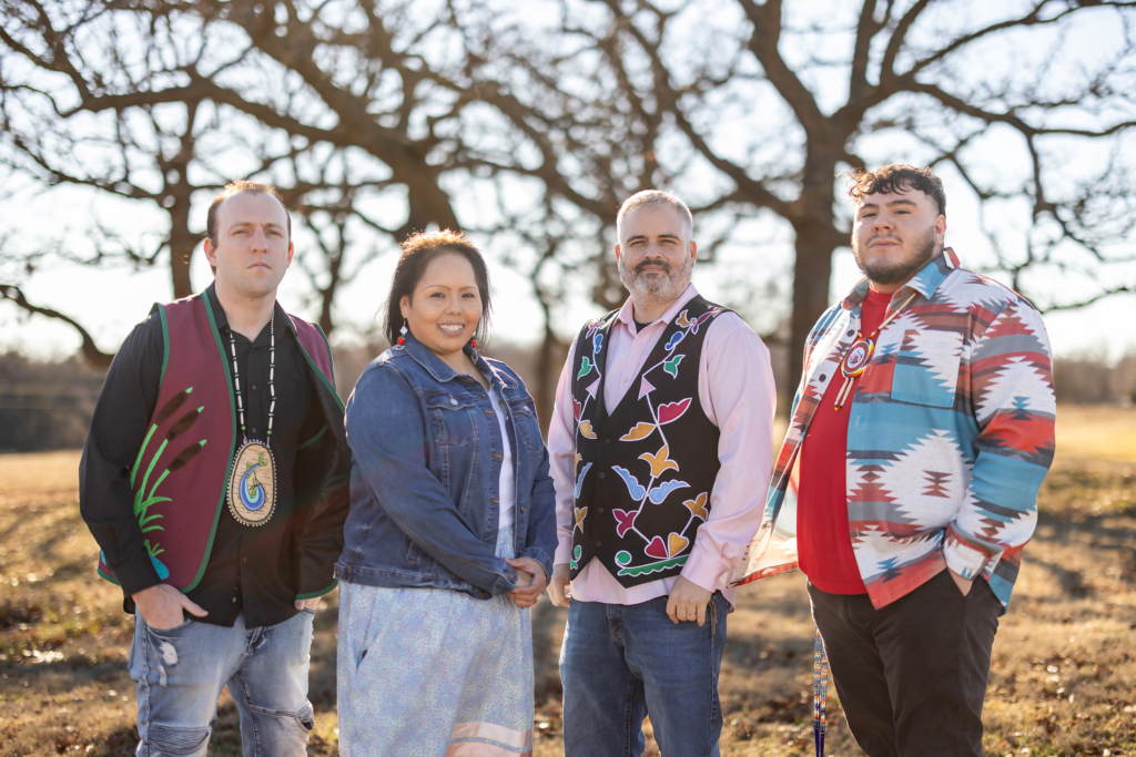 A group of four staff members wearing applique vests and jackets stand together outside in winter sun.