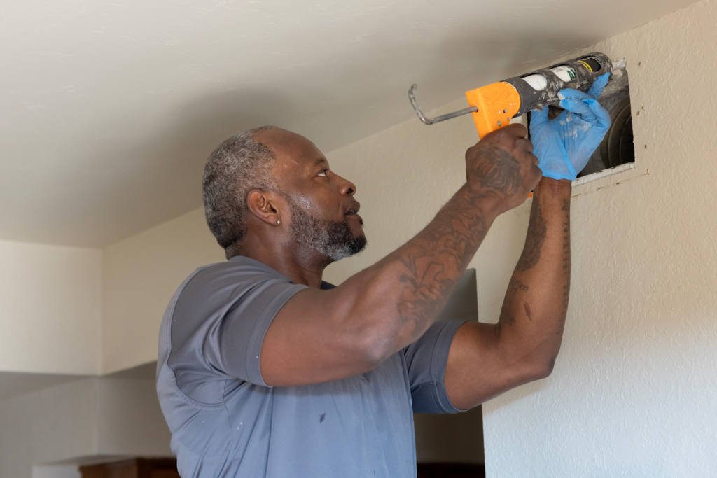 A worker seals a duct in a home.