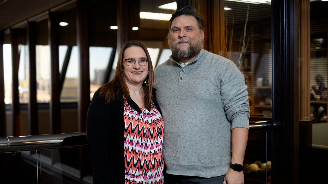 Randy Haas and his wife Melissa pose for a photo at their offices in Oklahoma City, Tuesday, Dec. 21, 2021. Randy wears a grey pullover shirt and has a brown beard. His wife Melissa wears a brightly colored shirt with a zigzag pattern on it, and wears glasses.