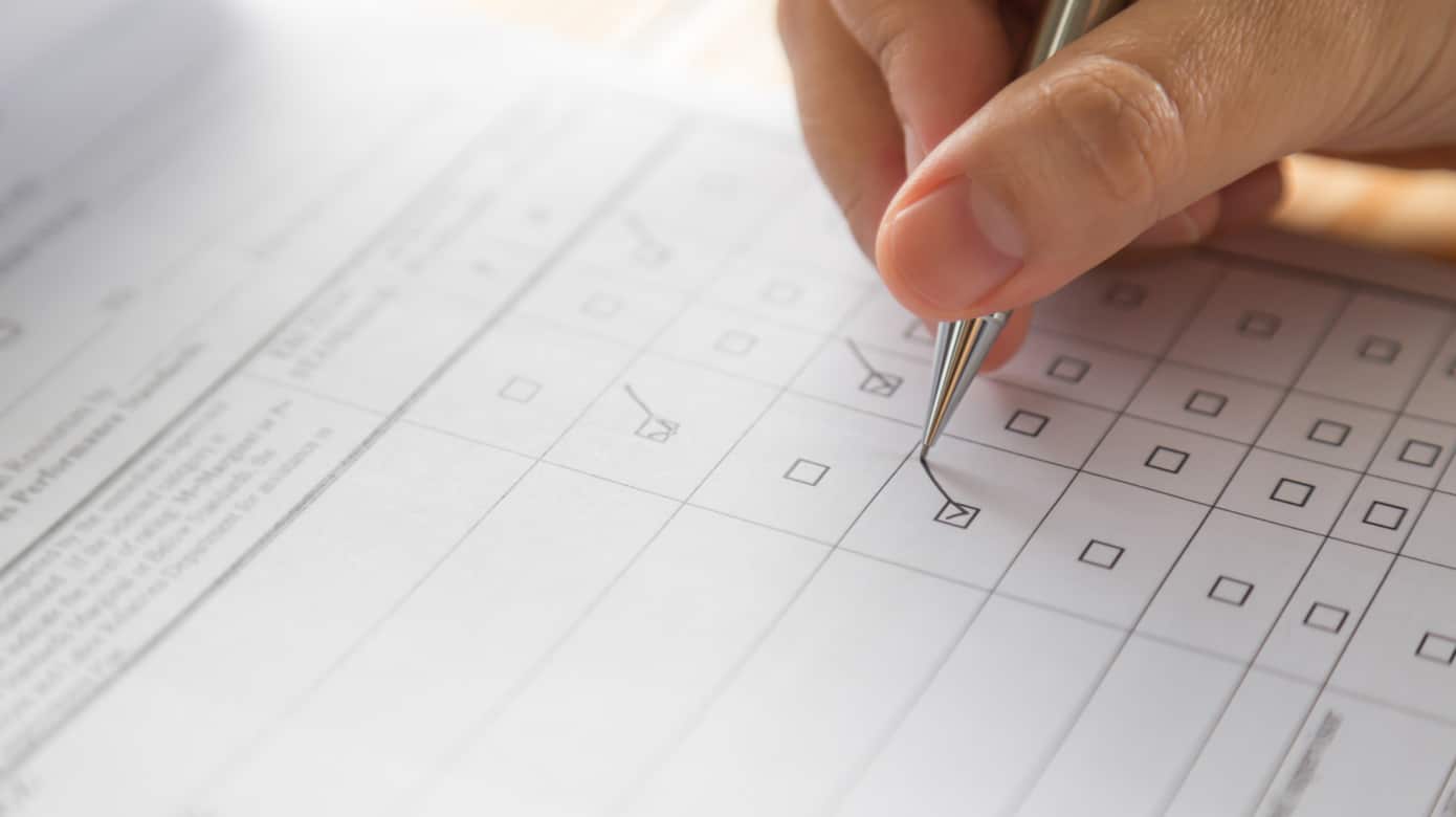 Close-up of a hand holding a pencil and checking a box on a multiple-choice form.