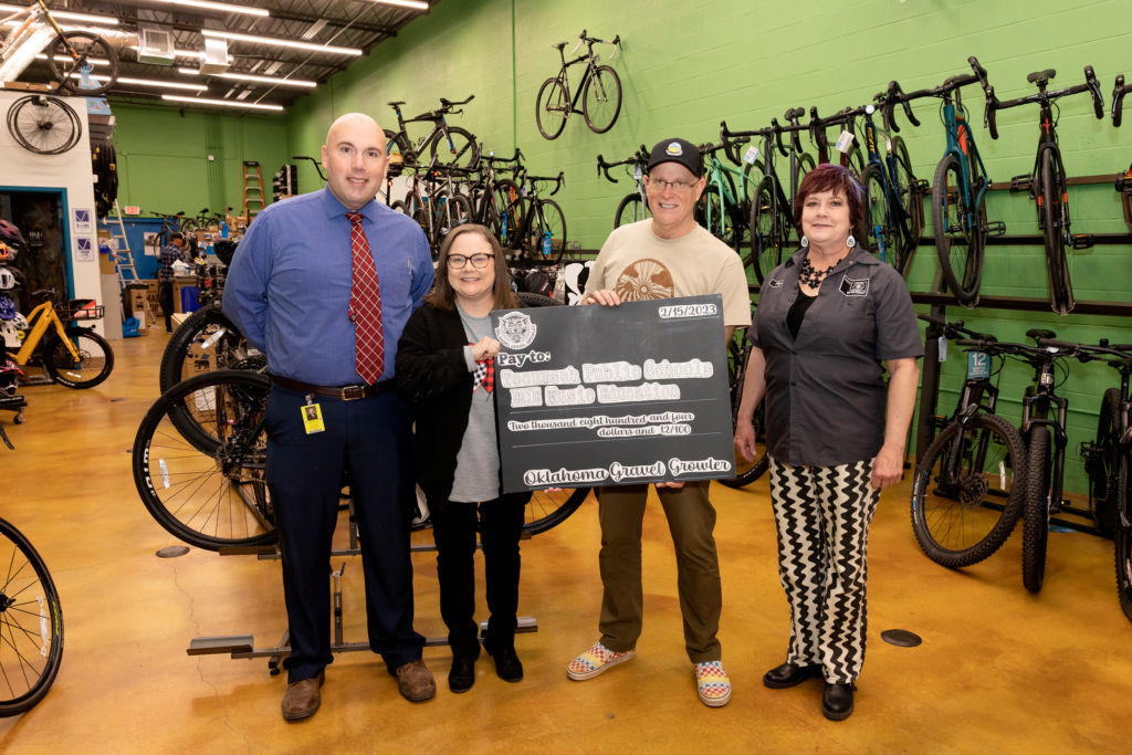 Organizers of the Gravel Growler bike race and Tecumseh Public Schools staff pose inside the spOKeLAHOMA bike shop with a display check of $2,804.12 in proceeds that will benefit the Tecumseh Early Childhood Center's music education program.