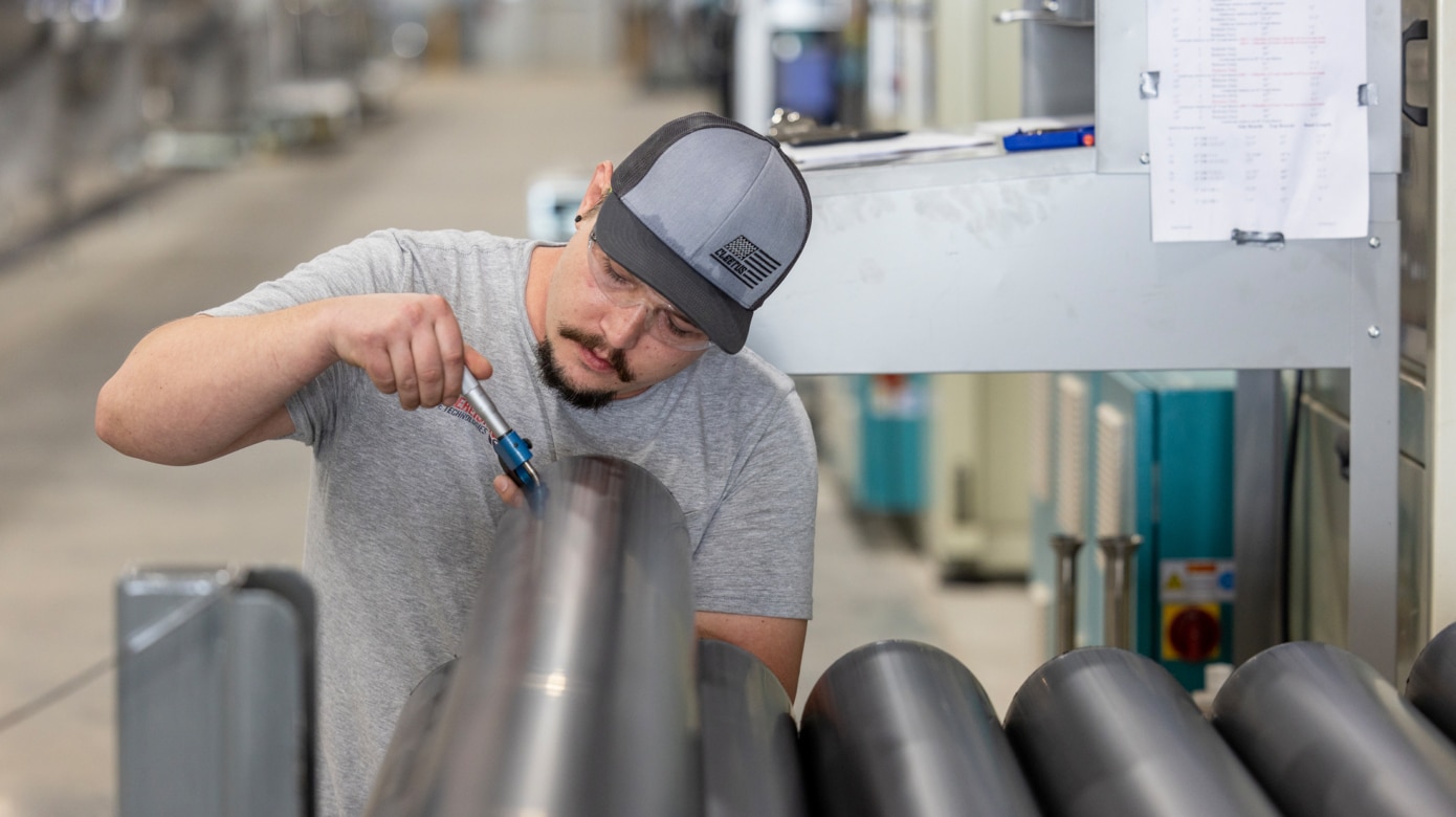 An employee wearing a grey t-shirt and grey ball cap examines a stack of pipe at CPN's Sovereign Pipe Technologies.