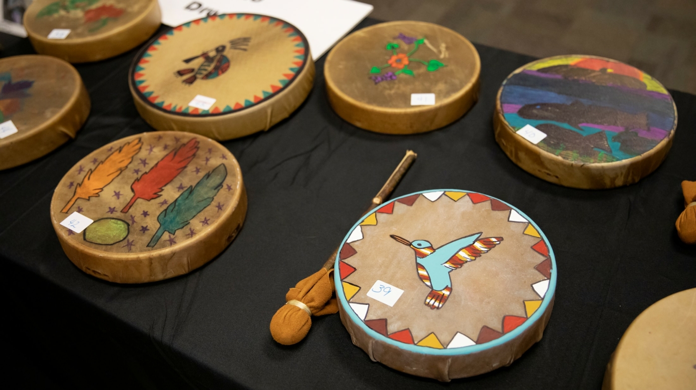 Painted hand drums with birds, feathers and other designs are grouped on a table following a JOM activity.
