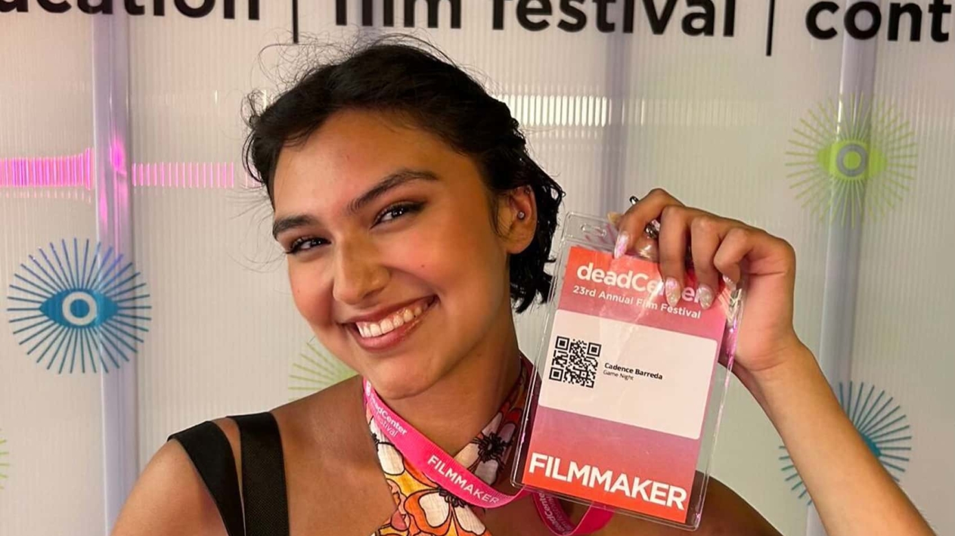 Cadence Barreda wears a floral shirt and holds up her credentials for the DeadCenter Film Festival.