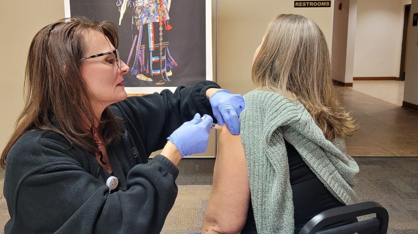 A nurse wearing blue medical gloves gives a vaccination to a participant in a green sweater at a recent vaccination education event.